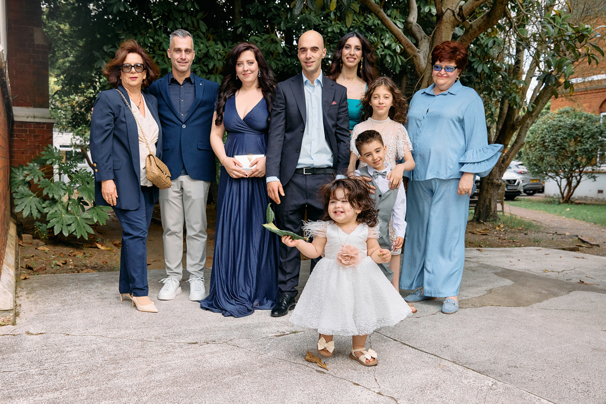 A group of family standing looking at a little girl walking in ther new dress after her christening.