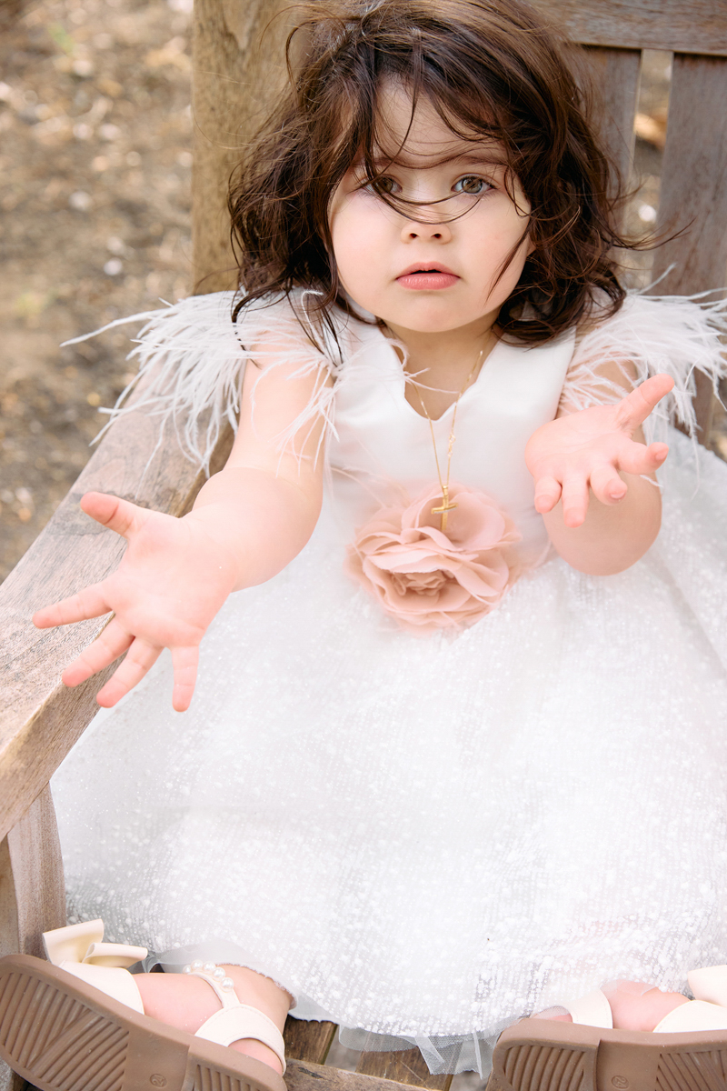 Little girl ini her christening dress sitting on a bench outside a church.