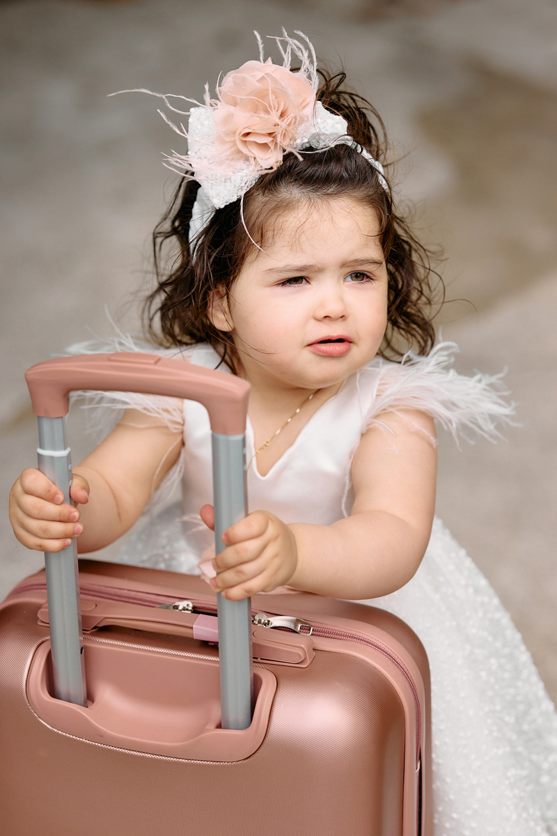 Little girl ini her christening dress holding a pink suticase.