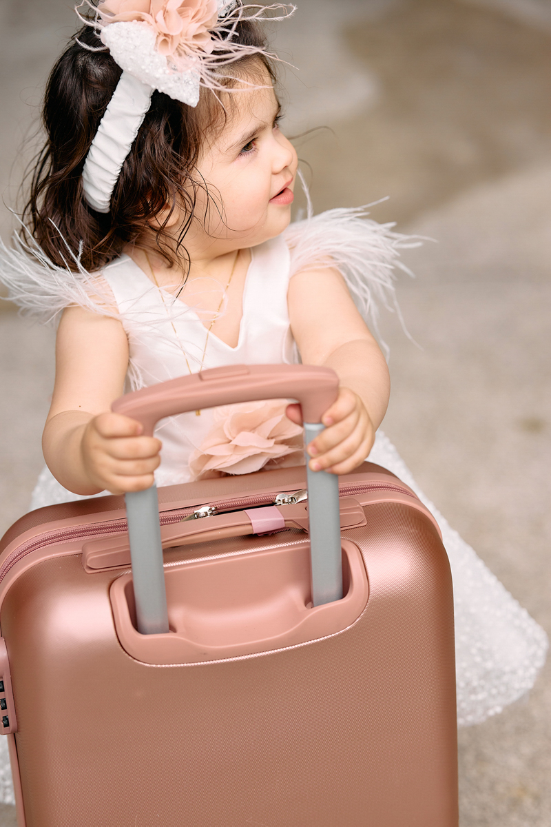 Little girl ini her christening dress holding a pink suticase.