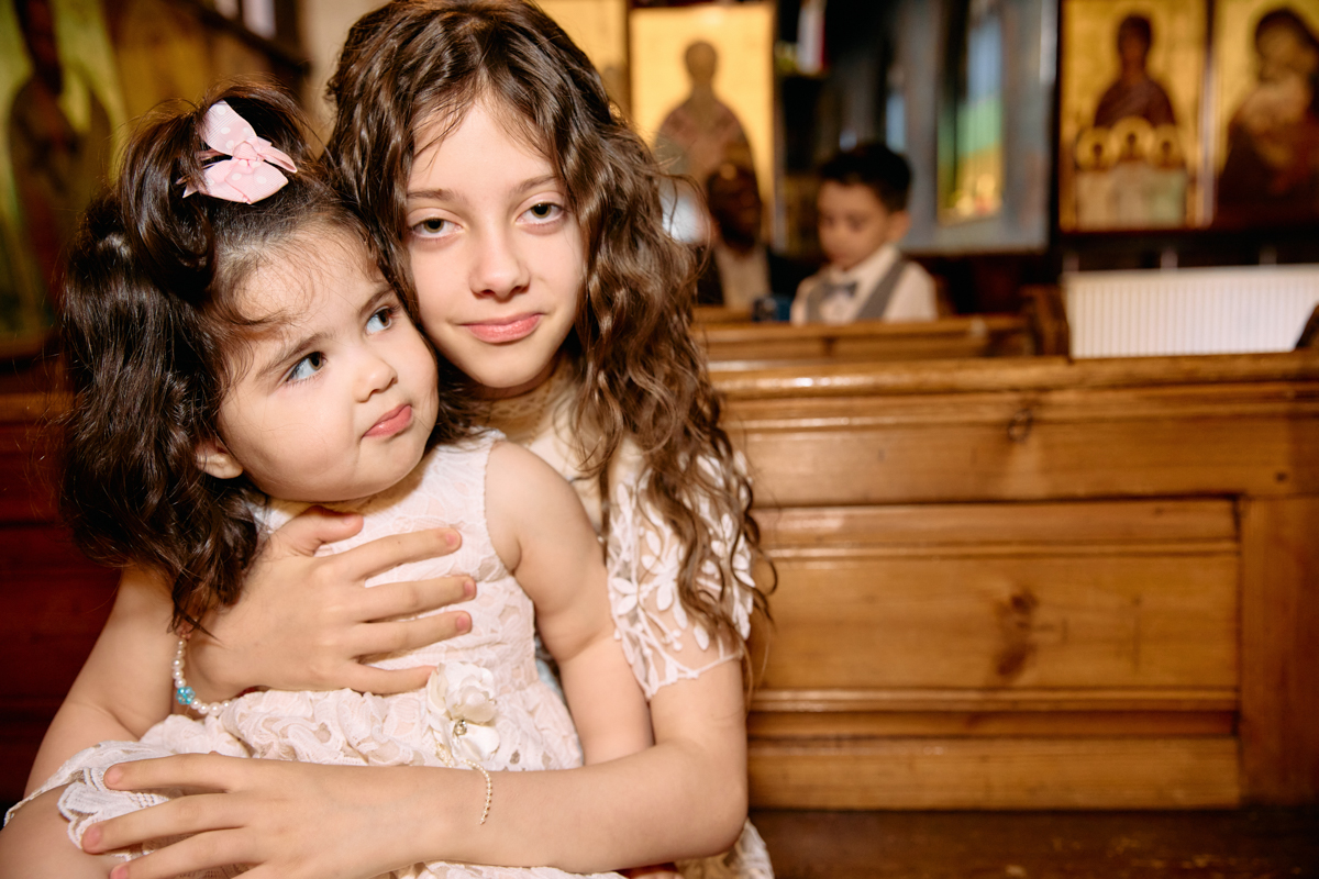 A little girl hugging her little sister who is about to be baptised in a church.