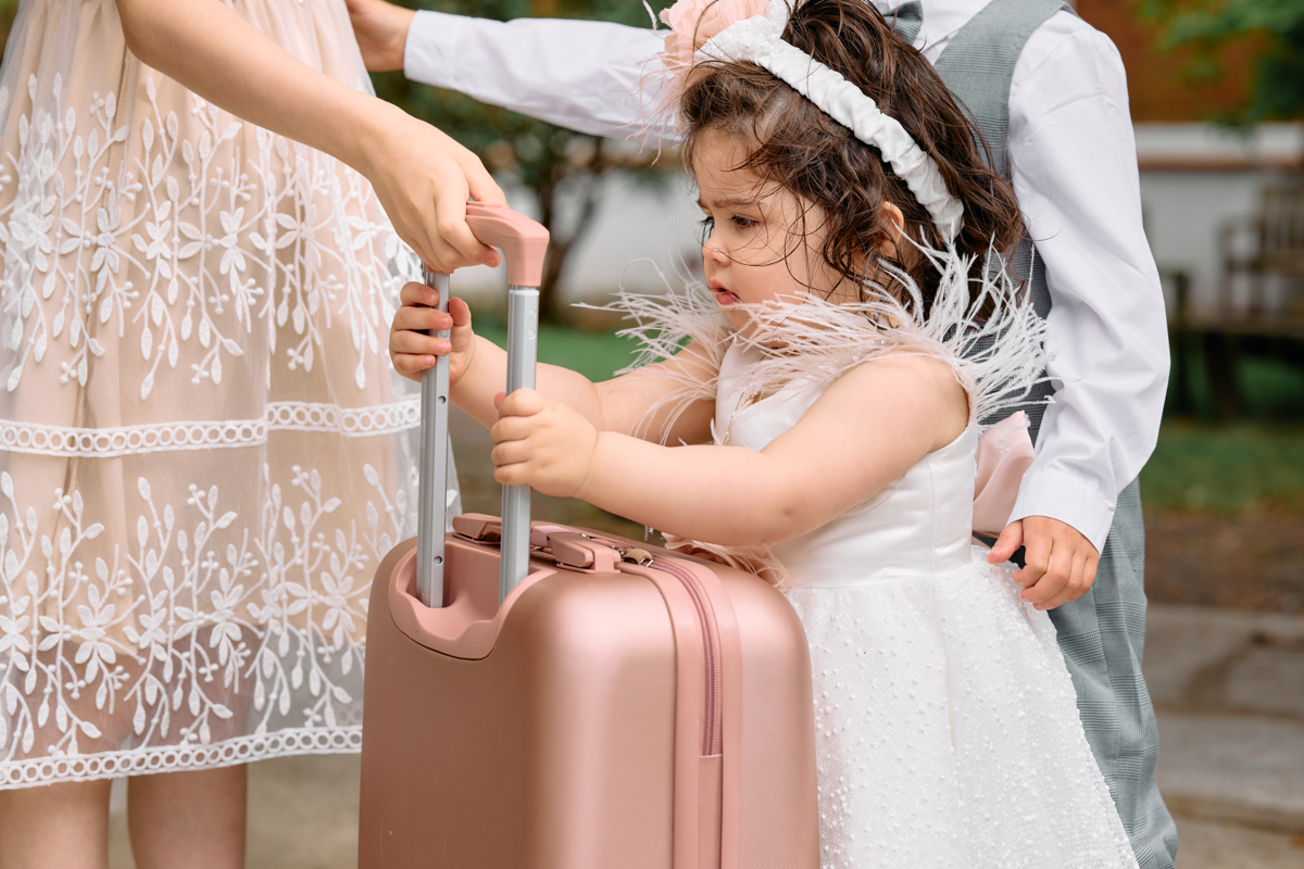 Little girll in her new christening dress after her christening outside the church holding a pink suitcase.