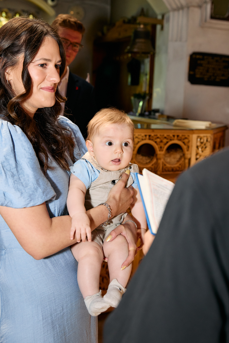 Godmother holding a baby while a priest is reading the blessings.