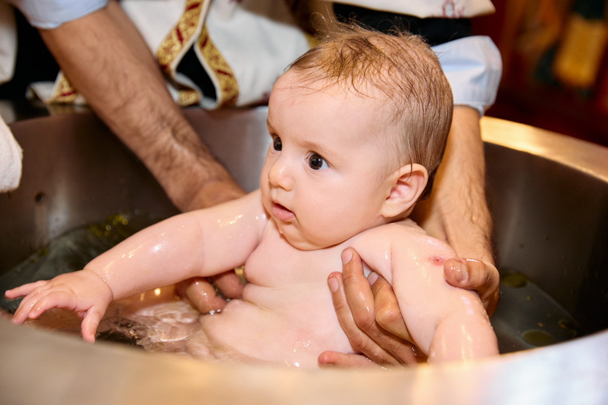 Baby being gently bathed in holy water at the font.