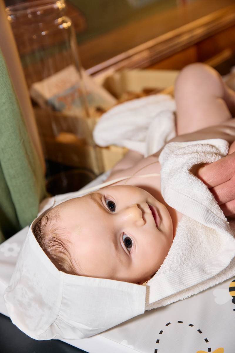 Baby lying down, eyes open, wrapped in white cloth.