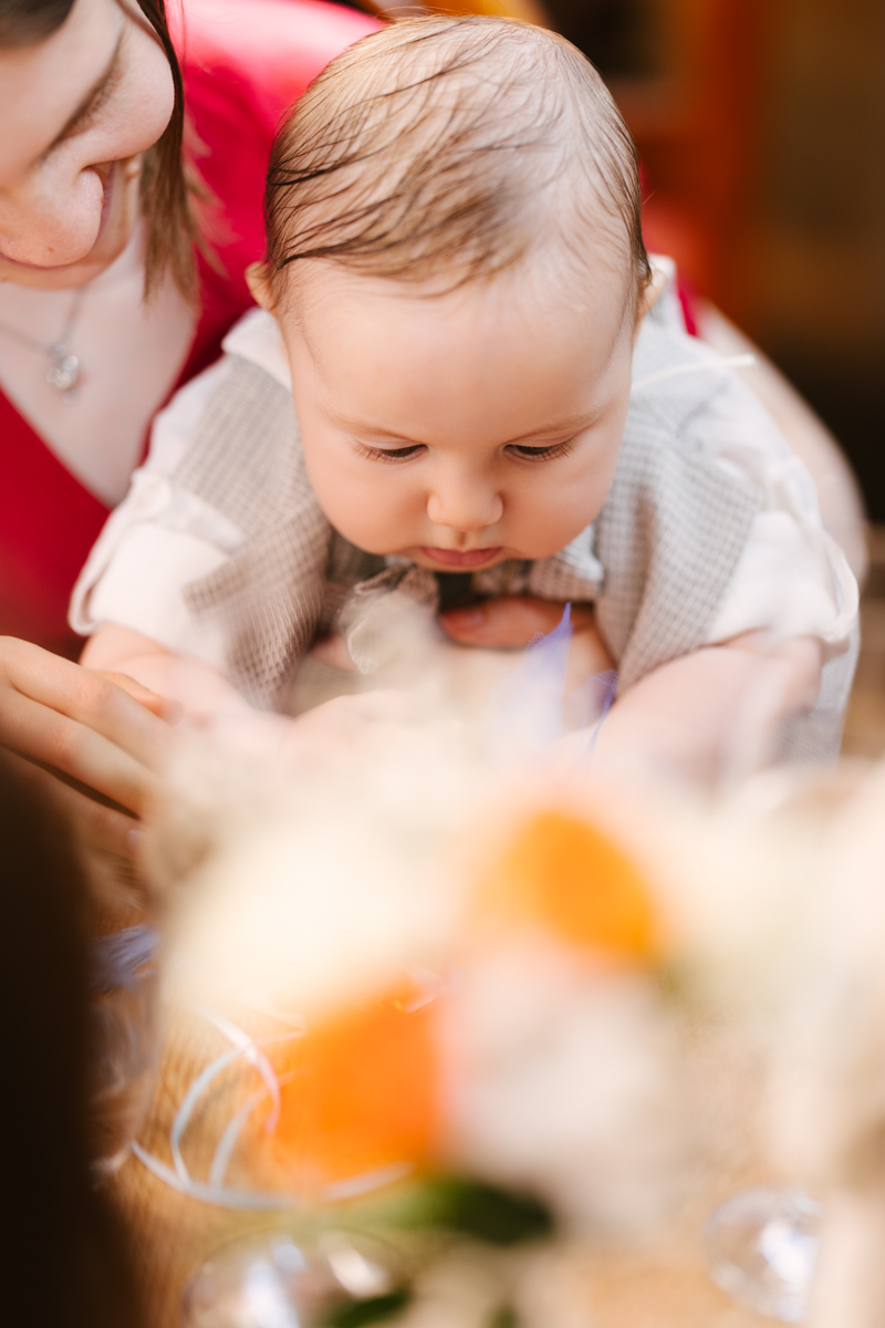 Baby leaning forward to look at flowers or food.