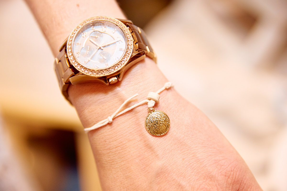 A close up of a hand wearing a watch and a christening bracelet.