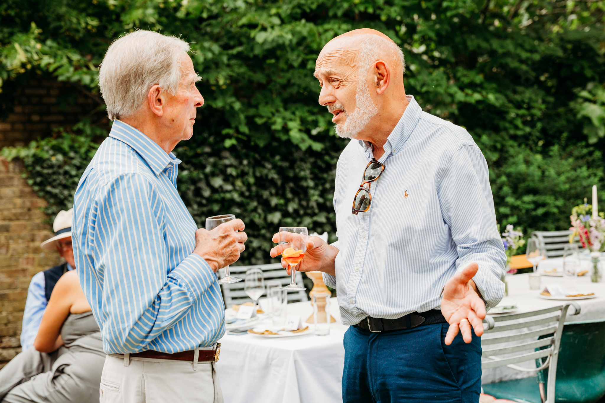 2 men conversing while having drinks at a party outdoors.