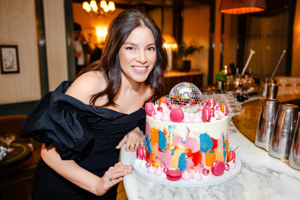 A lady in a black dress posing by her birthday cake.