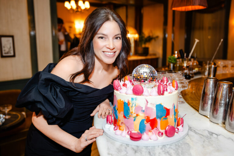 A lady in a black dress posing by her birthday cake.