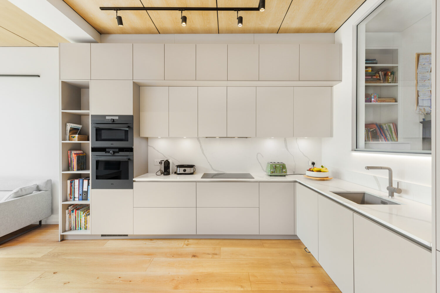 Modern handleless kitchen with light grey cabinetry, wooden worktops, wooden ceiling beams.