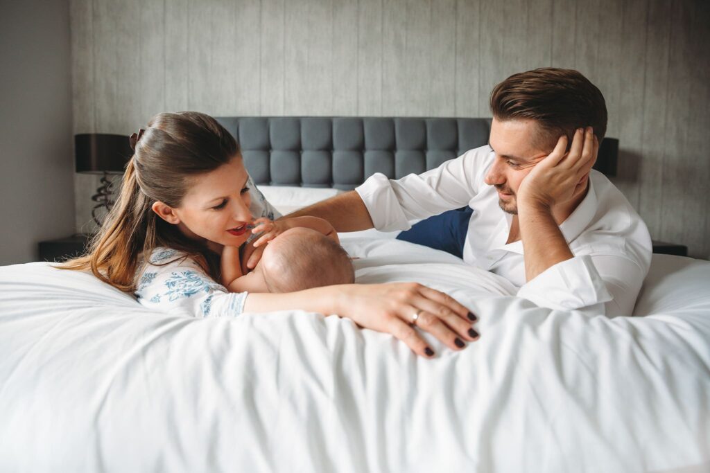 Mum and dad playing with their newborn baby in bed.