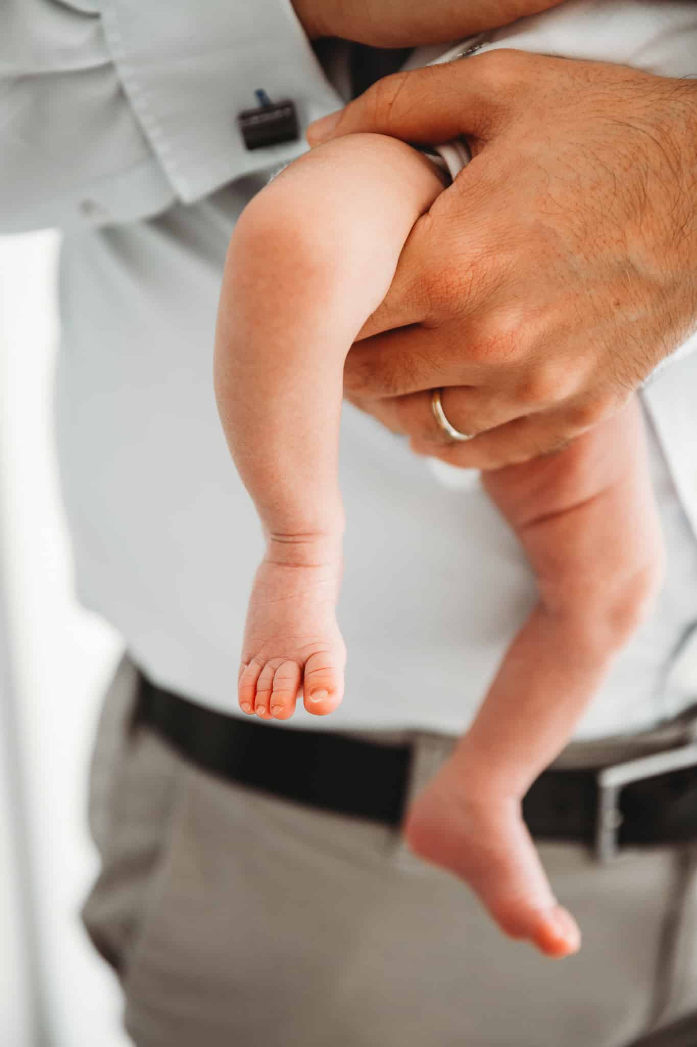 London family photography. Newborn baby legs held by dad in a close up shot.