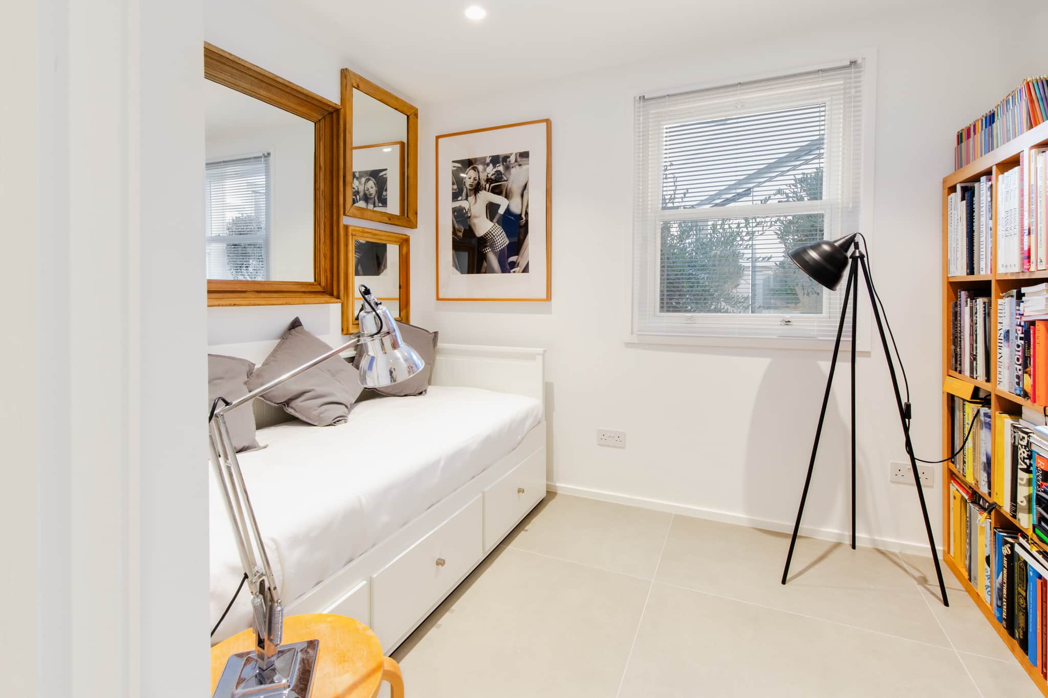 Light filled bedroom with daybed, wooden shelving, framed artwork, large window.