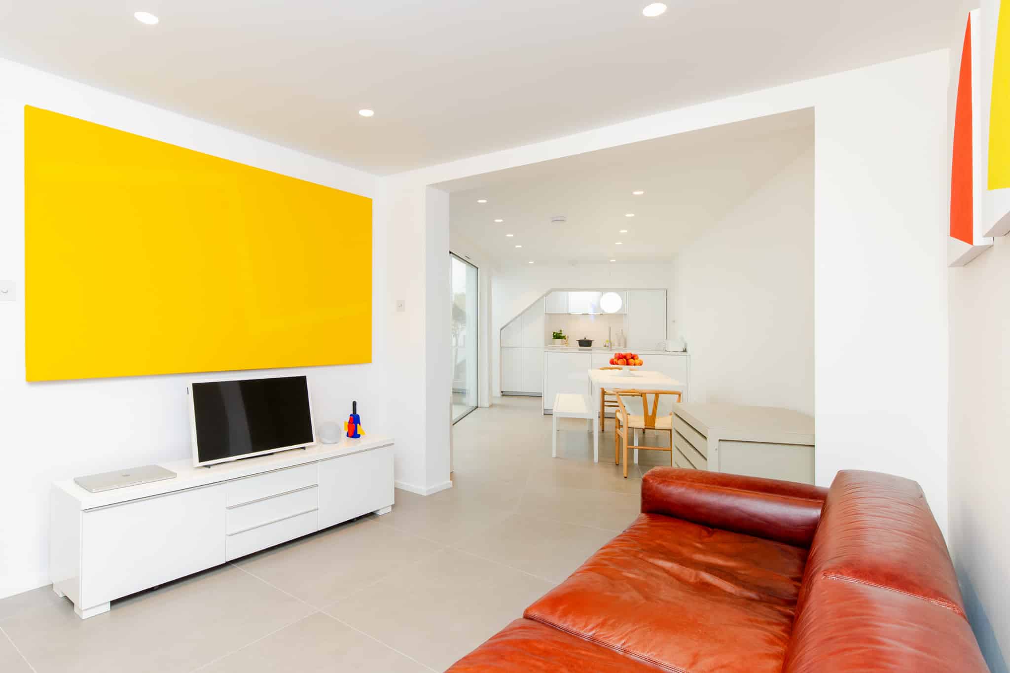 Contemporary living room with bold yellow accent wall, leather sofa, white TV unit.