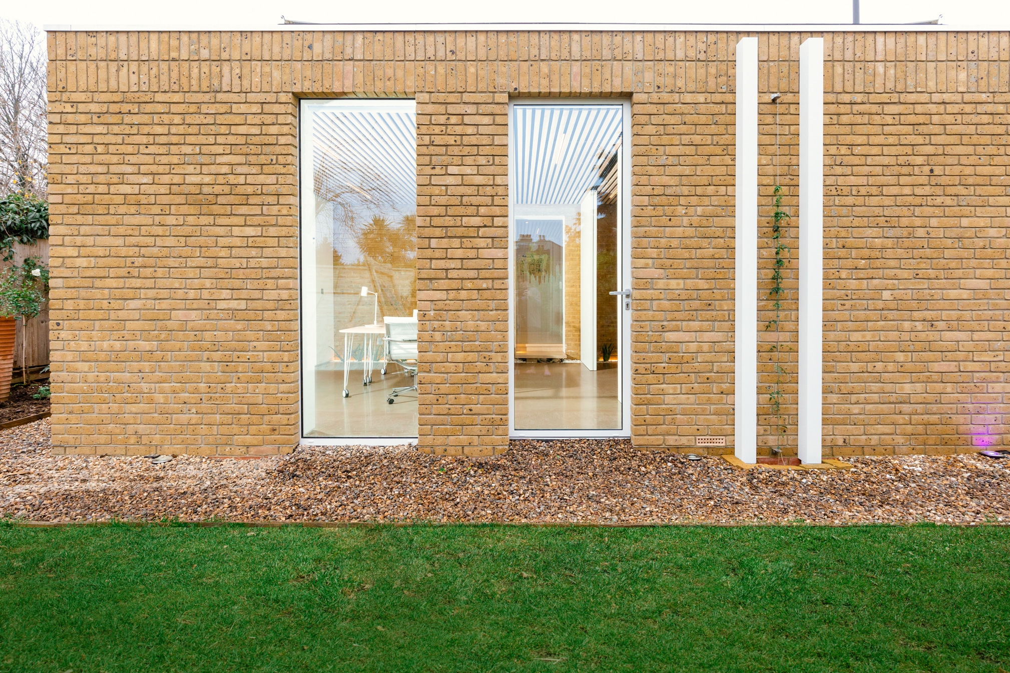 External view of modern brick house extension with large windows, neat green lawn.