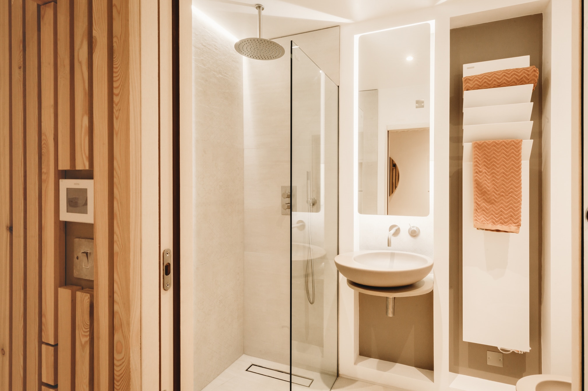 Interiors photography. Contemporary bathroom with wooden slat wall, glass shower enclosure, white vanity unit.