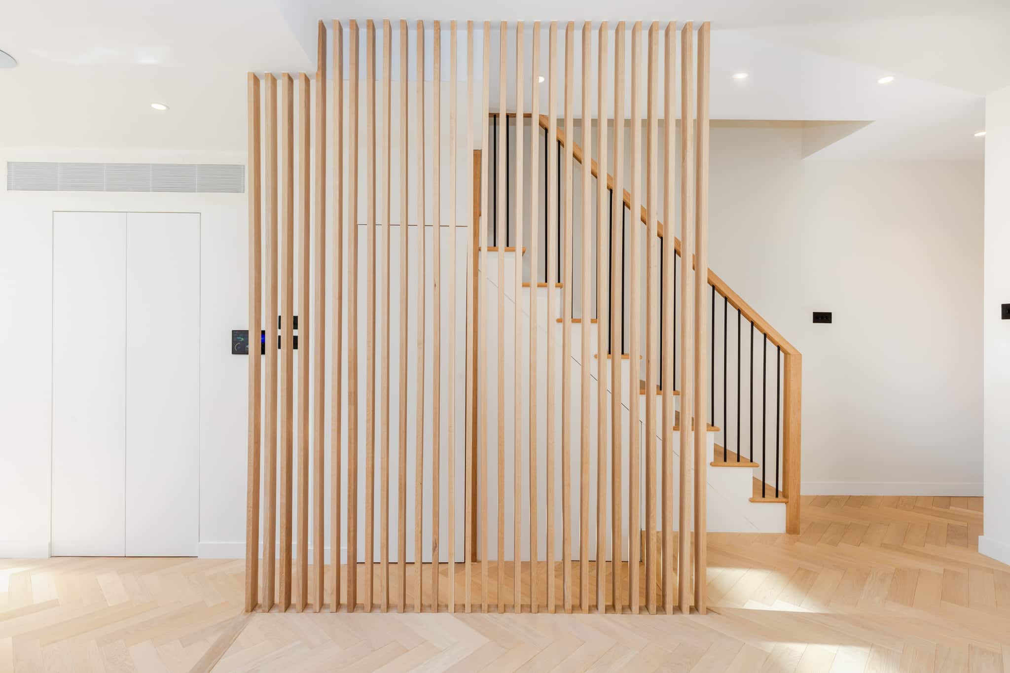 Bright hallway with white staircase, vertical oak slat wall paneling, white walls.