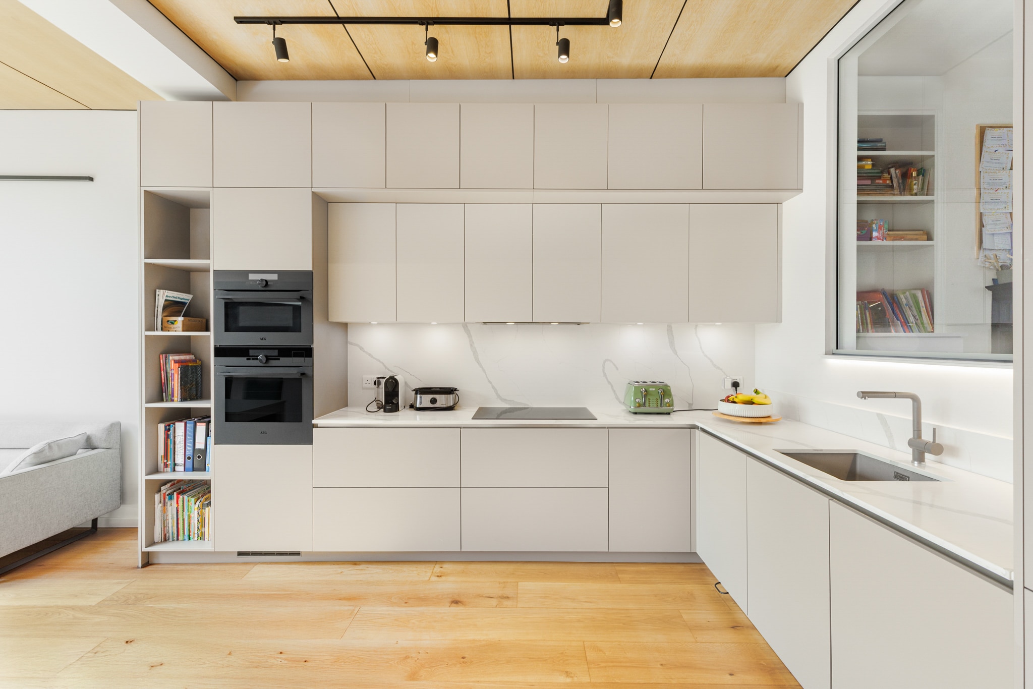 Modern handleless kitchen with light grey cabinetry, wooden worktops, wooden ceiling beams.
