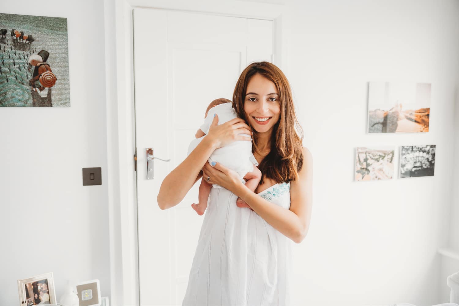 Mum in white nightie holding her newborn baby while looking at the camera.