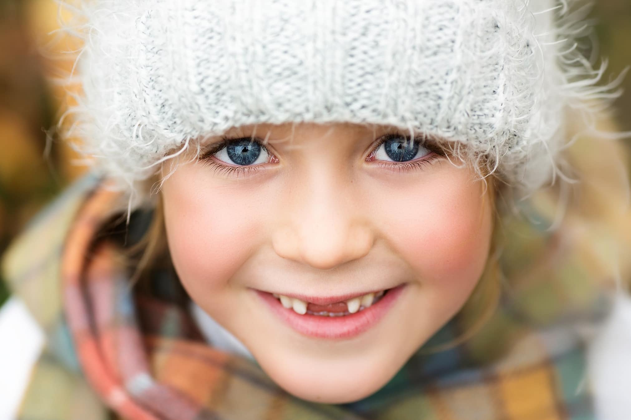 Little girl with beautiful blue eyes and missing teeth looking at the camera and smiling.